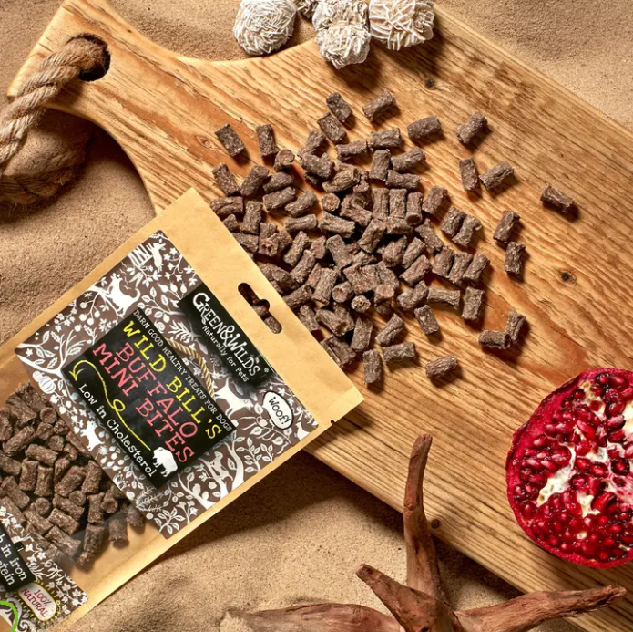Dog treats on a wooden board with packaging, surrounded by natural elements.