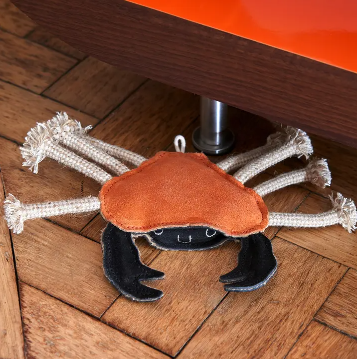 Green & Wild's Carlos the Crab eco dog toy, a rope orange crab toy placed on a wooden floor 