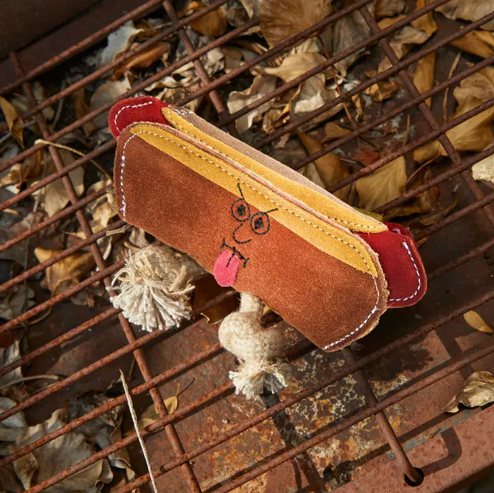 Green & Wild's Harry the Hotdog eco dog toy, with small rope knots attached, pictured on a metal grate