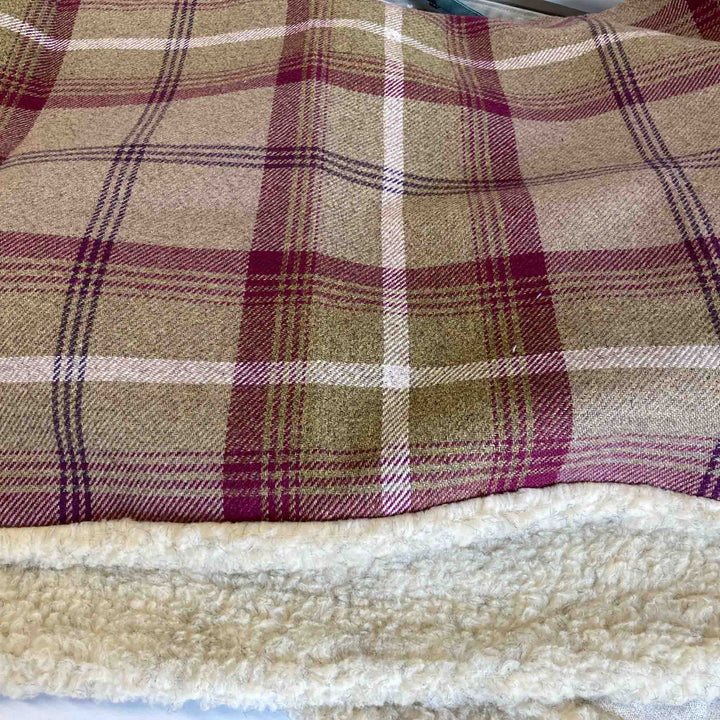 A close-up of a plaid woven blanket or throw with a soft sherpa fleece backing. The top portion shows the plaid pattern in beige, olive green, burgundy, and white, while the bottom portion shows the cream-colored fleece texture.