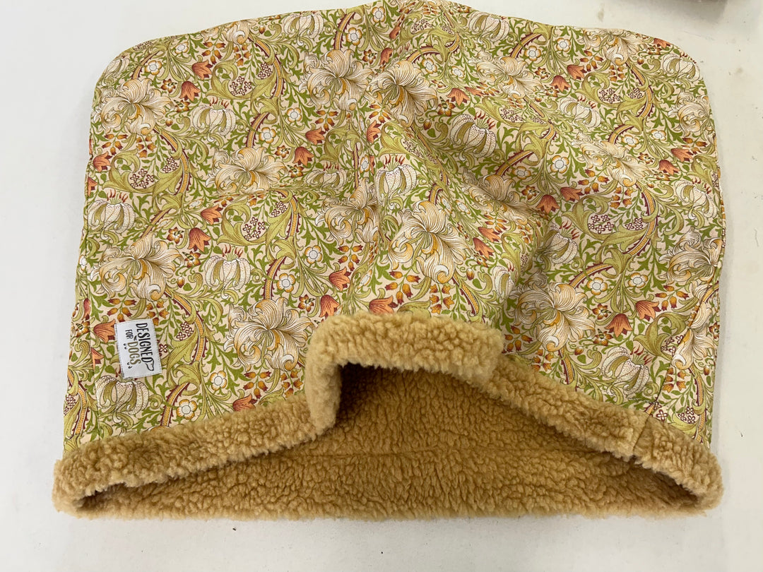 A fabric-covered pet bed with a floral print in sage green, cream, and orange, featuring a plush tan fleece lining and a small sewn-in label that reads 'BARNES'.