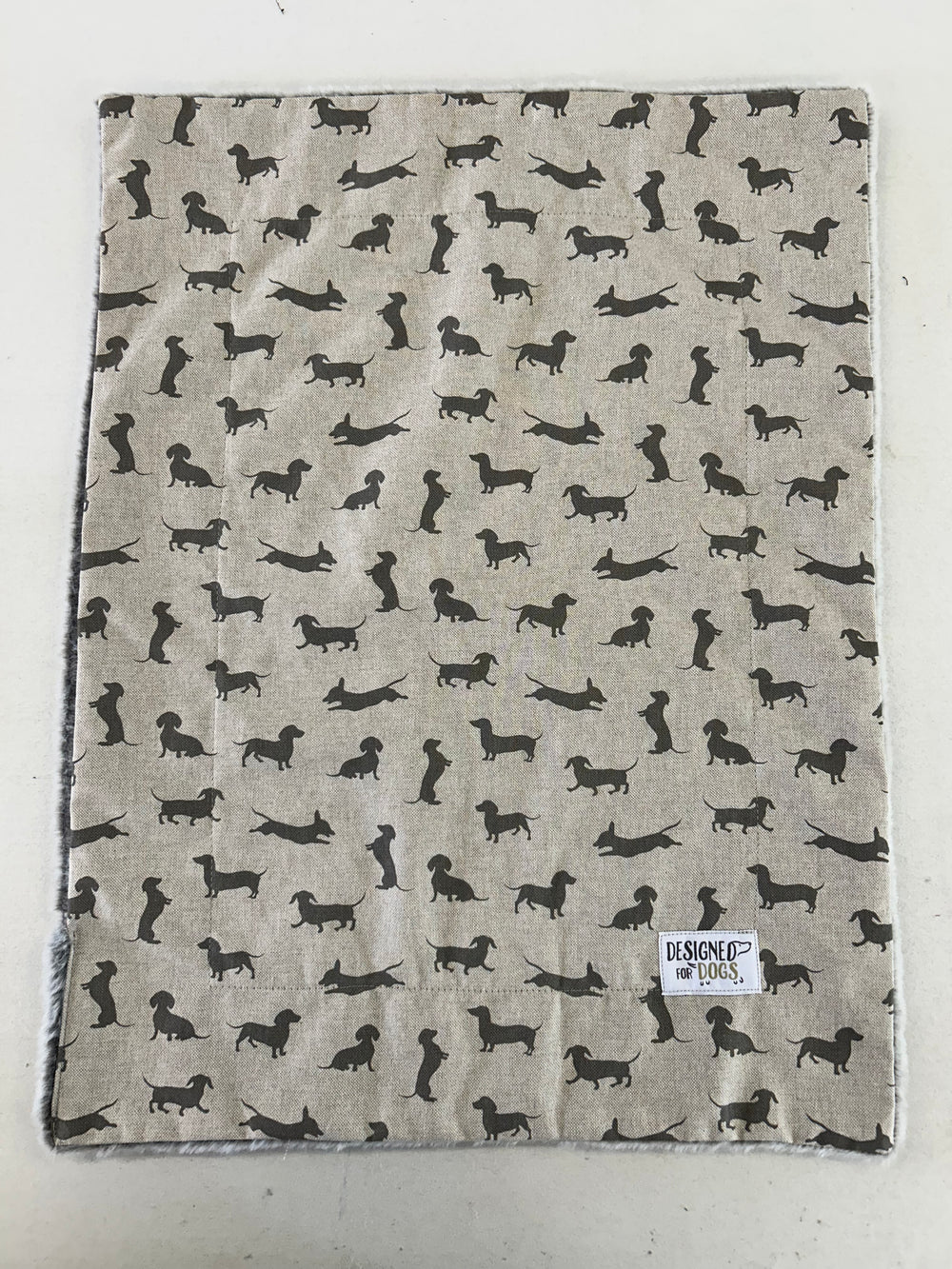 A square fabric item, likely a blanket or towel, featuring a repeating pattern of black dachshund dog silhouettes on a light beige linen-like background. A small white label reading 'HESPOE of HOUS' is visible in the bottom right corner.