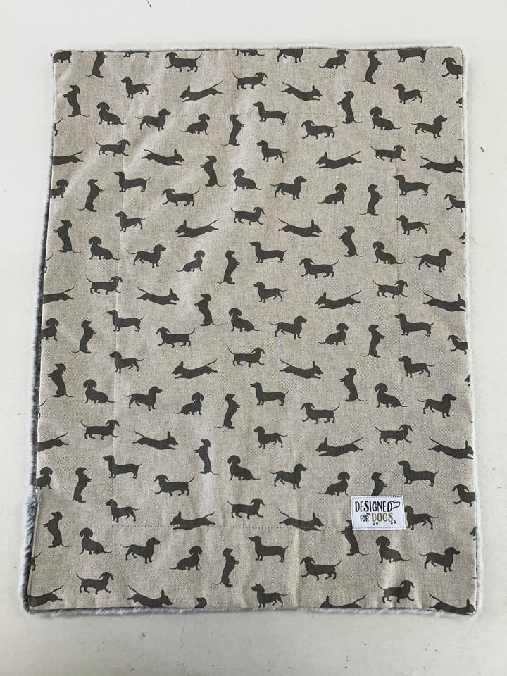 A square fabric item, likely a blanket or towel, featuring a repeating pattern of black dachshund dog silhouettes on a light beige linen-like background. A small white label reading 'HESPOE of HOUS' is visible in the bottom right corner.