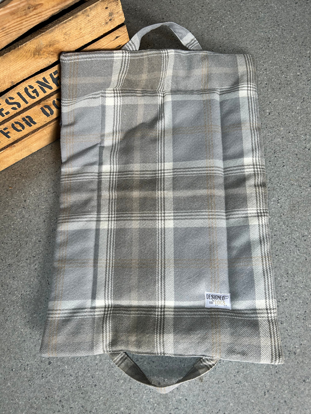 A gray and white plaid fabric bag with two top handles, laid flat on a gray textured surface next to a wooden crate.