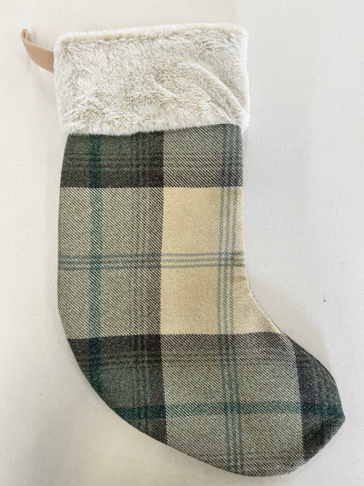 A Christmas stocking featuring a green and beige plaid wool body with a fluffy cream faux-fur cuff and a hanging loop.