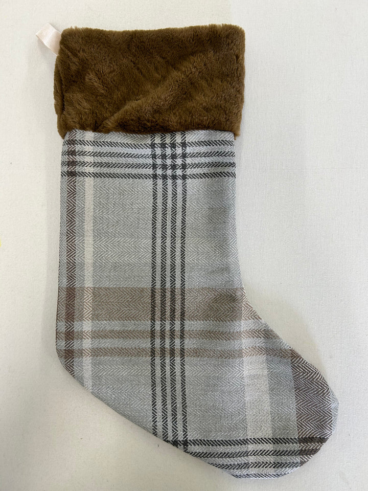 A Christmas stocking with a brown faux fur cuff and a gray, white, and black plaid fabric body, shown against a plain off-white background.