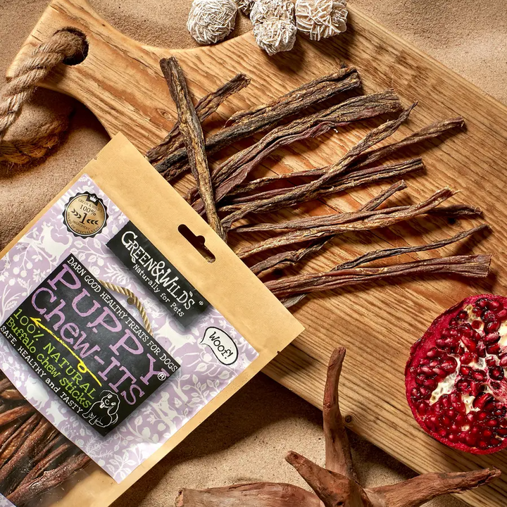 Green & Wild's puppy chew-its packaging on a chopping bpard with a pomegranite 