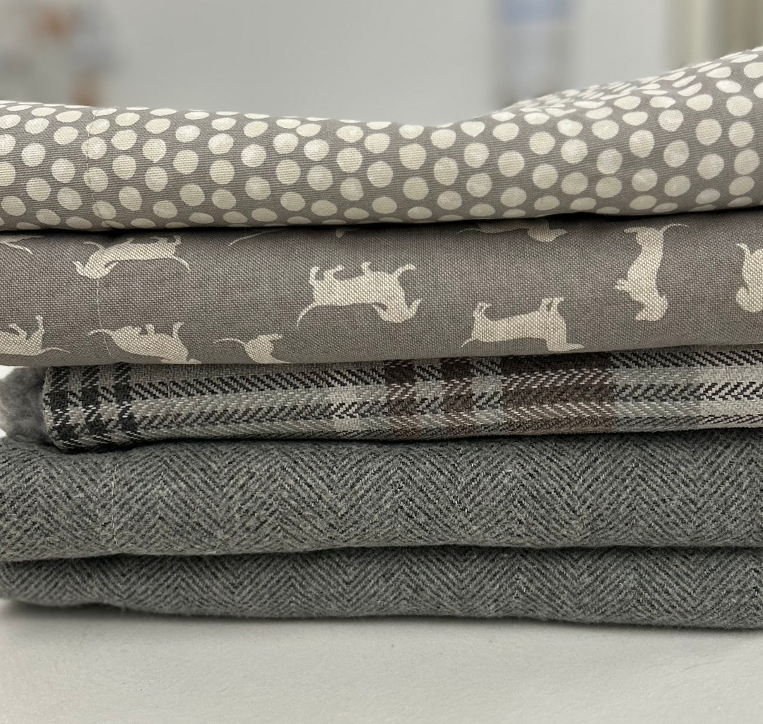 Stack of grey snuggle sacks in various fabrics, including spotty, dachshund, tweed and tartan. 