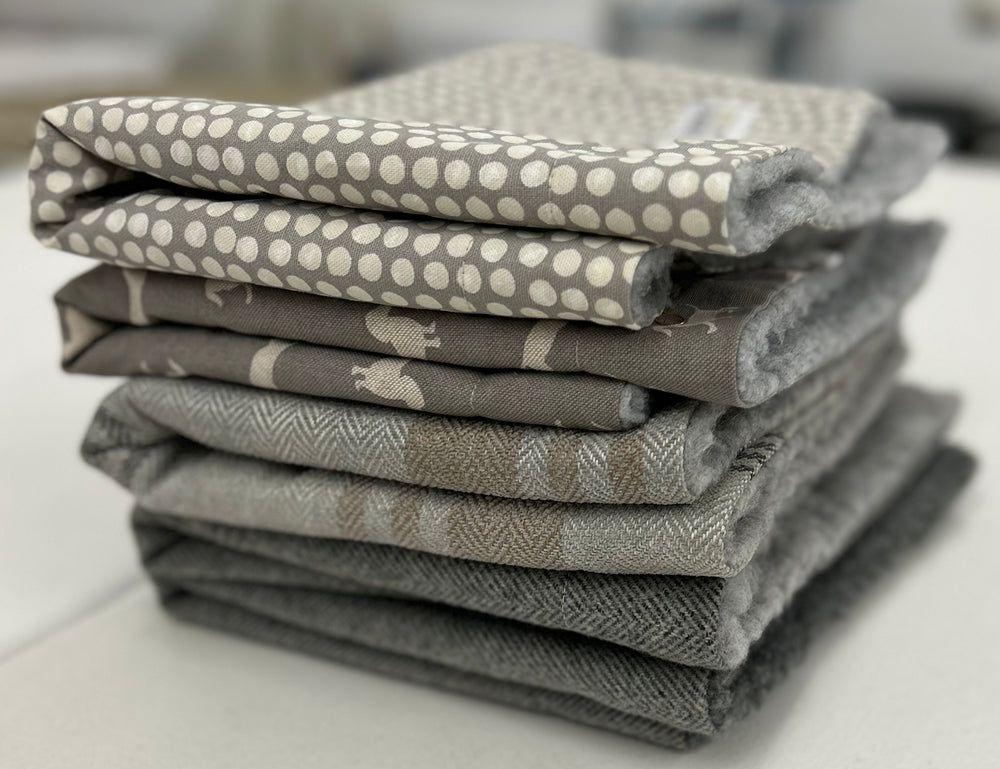 Stack of grey snuggle sacks in various fabrics, including spotty, dachshund, tweed and tartan. 