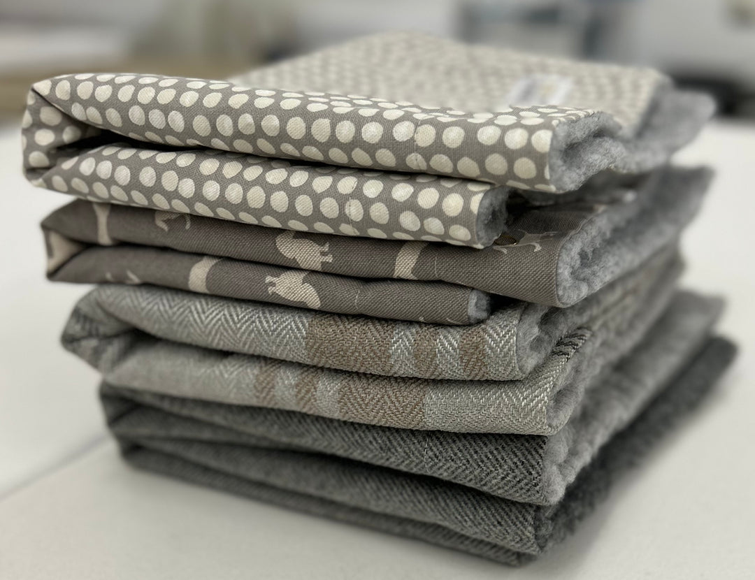 Stack of grey snuggle sacks in various fabrics, including spotty, dachshund, tweed and tartan. 
