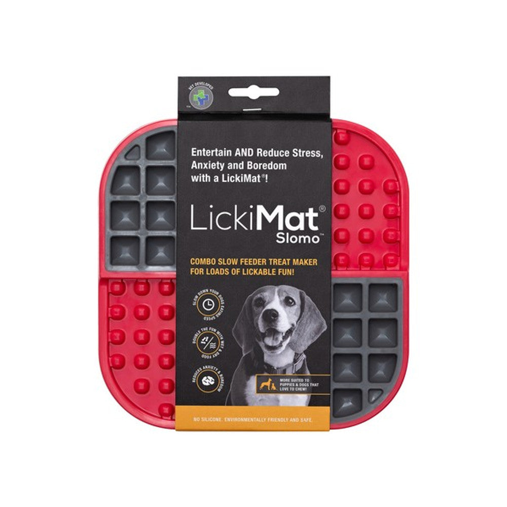 A red LickiMat slow feeder mat for dogs, featuring raised dots for food placement, with a product label and a dog image on the upper part of the packaging.