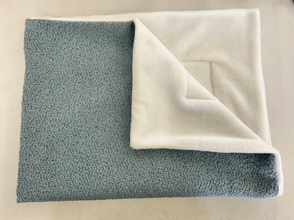 Blue bouclé fabric blanket with white inside, folded for the image 