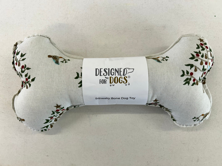A bone-shaped dog toy made of light beige fabric with a floral print and a white paper label in the center that reads 'DESIGNED FOR DOGS Squeaky Bone Dog Toy'.