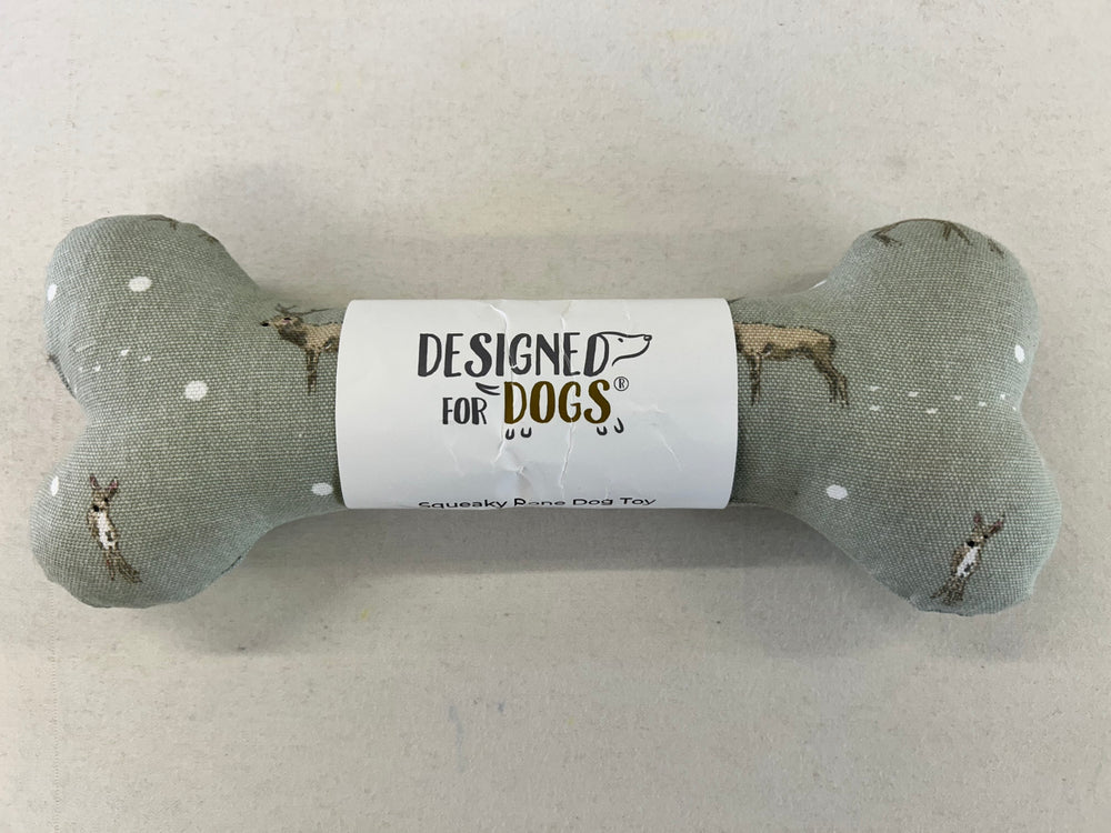 A bone-shaped dog toy made of textured gray fabric with small white dots and printed dog illustrations, wrapped in a white paper band that reads 'DESIGNED FOR DOGS'.