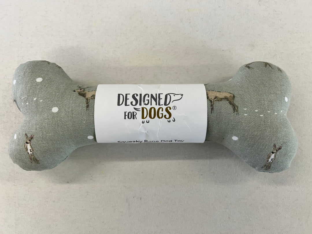 A bone-shaped dog toy made of textured gray fabric with small white dots and printed dog illustrations, wrapped in a white paper band that reads 'DESIGNED FOR DOGS'.