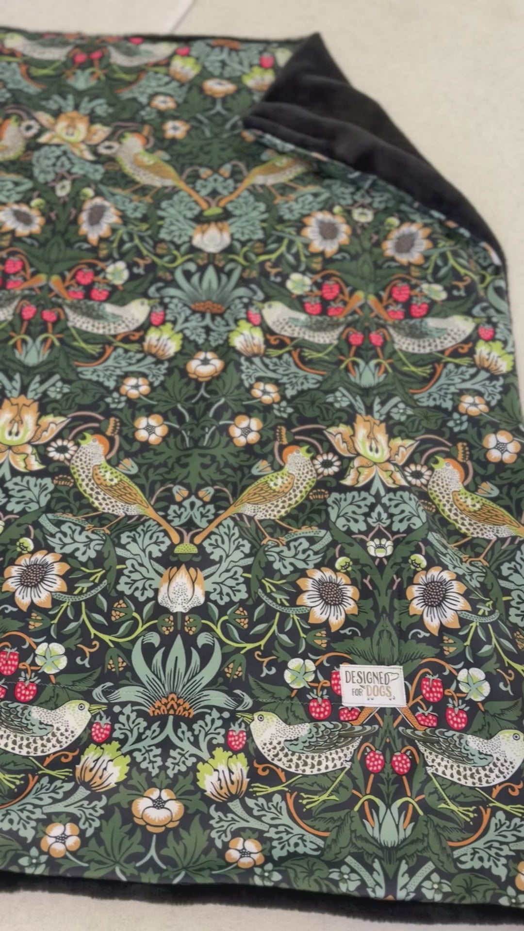 Blanket in the William Morris Strawberry thief blanket on a wooden floor. Fabric shows birds and flowers, with green/blue colours. VIDEO
