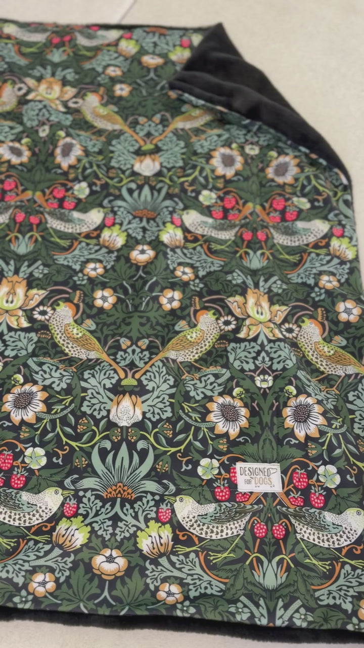 Blanket in the William Morris Strawberry thief blanket on a wooden floor. Fabric shows birds and flowers, with green/blue colours. VIDEO