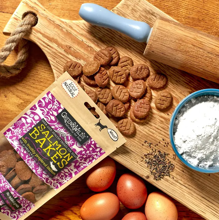 Green & Wild's salmon bakes packaging placed on a chopping board with a rolling pin, flour, seeds and eggs.