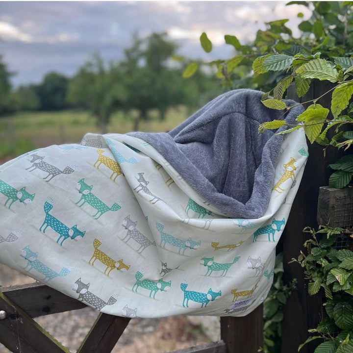 Snuggle sack in teal colours with fox patterns. Shown on a gate